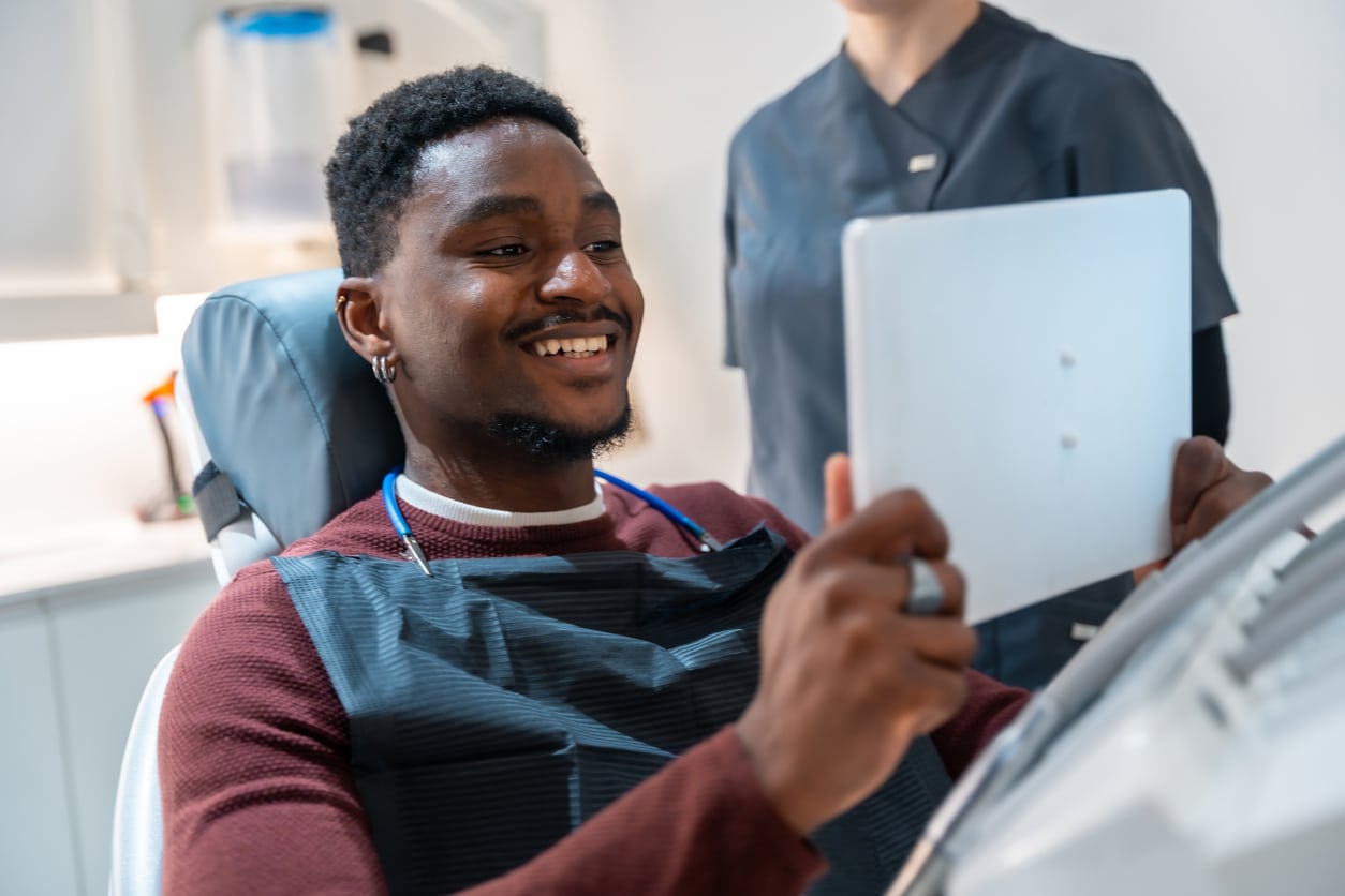 Young man smiling looking at results on tablet at dentist office